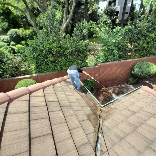Gutter cleaning job: worker pressure washing roof valley gutter, tiled roof